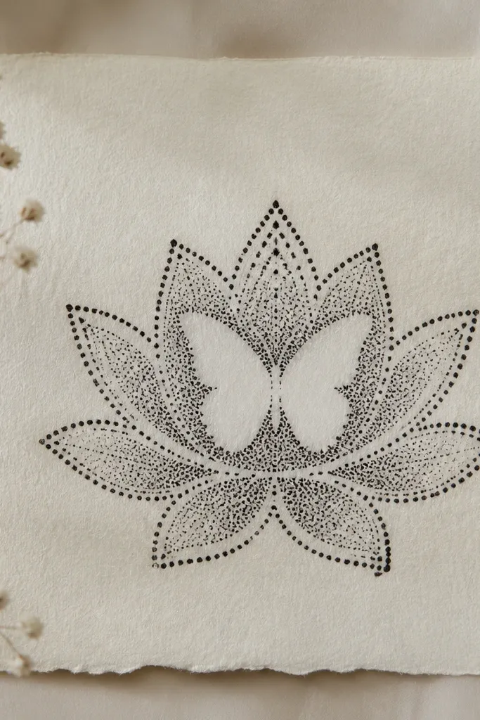 A stamped-looking lotus outline in black with repeated small petal dots along the petals. A butterfly is drawn in negative space - the wings are left uninked while the surrounding area is speckled with ink.