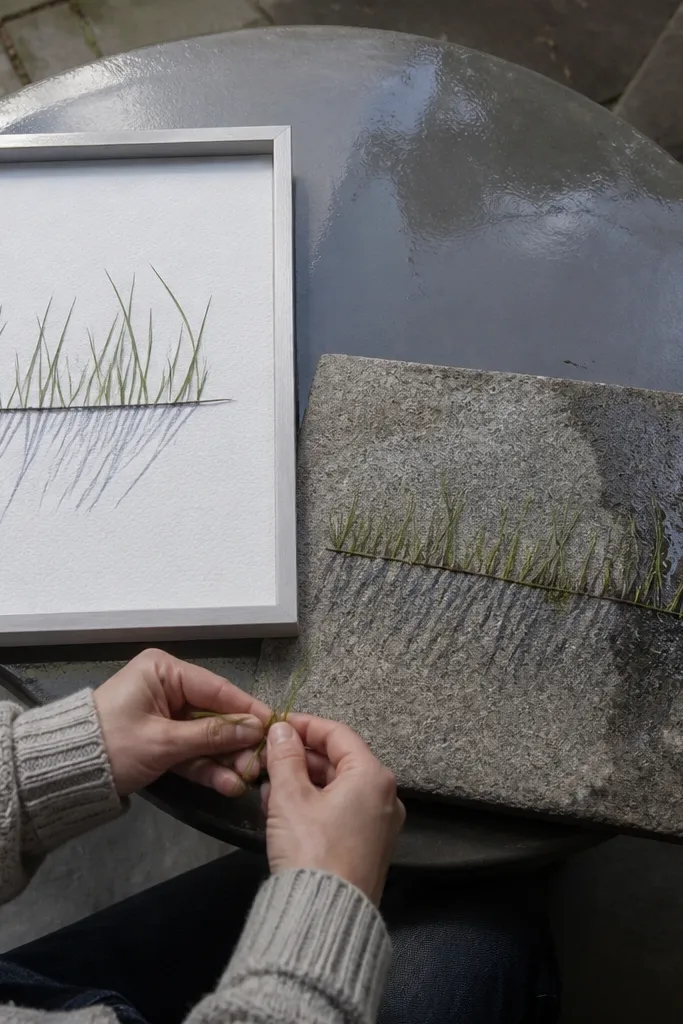 A low rock near the bottom with grass blades drawn in neat parallel lines. Under the grass is a rain-dark shadow band with faint streaks, all on a light background.